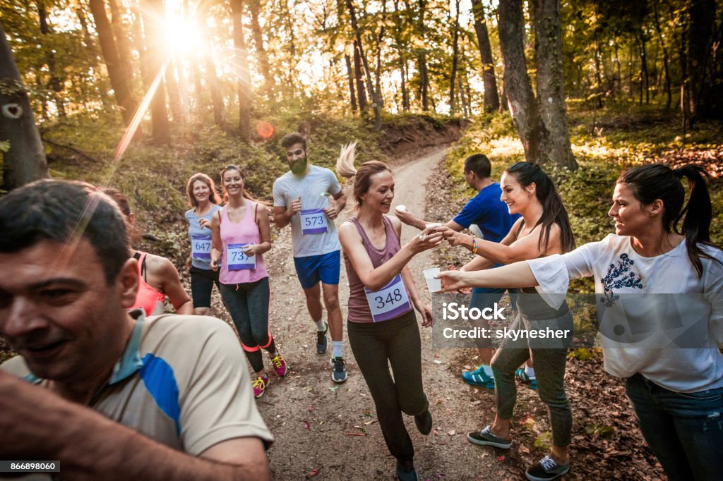 Volunteers passing fresh water to marathon runners during the race in nature. Large group of athletes refreshing themselves during marathon race. Volunteer Stock Photo