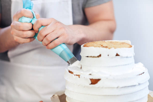 ペストリーの注射器を使用して白いクリームでケーキのクローズ アップ、装飾。男の手は、ケーキ生地にホイップ クリームを入れてください。 - buttercream ストックフォトと画像