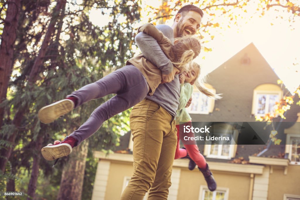 Father carrying daughters around neck.  Side view. Father carrying daughters around neck. Yard - Grounds Stock Photo