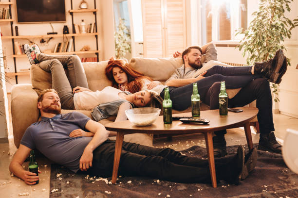 Group of wasted friends sleeping after party in the living room. Young drunk people resting with eyes closed at home. hangover stock pictures, royalty-free photos & images