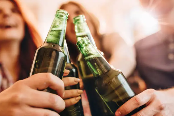 Close up of friends celebrating and toasting with beer bottles.