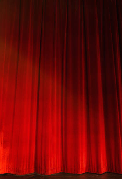 istock Red stage curtains, closed, lit by footlights 866912874