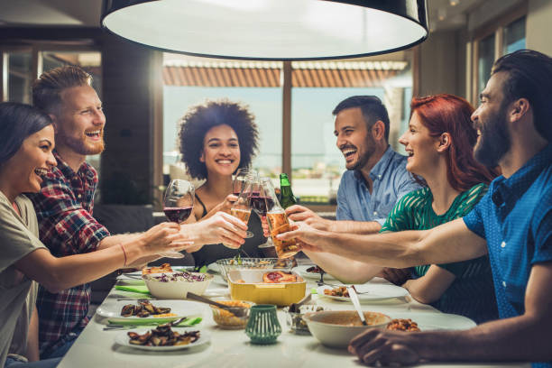 group of happy friends toasting while eating at dining table. - eating people group of people home interior imagens e fotografias de stock