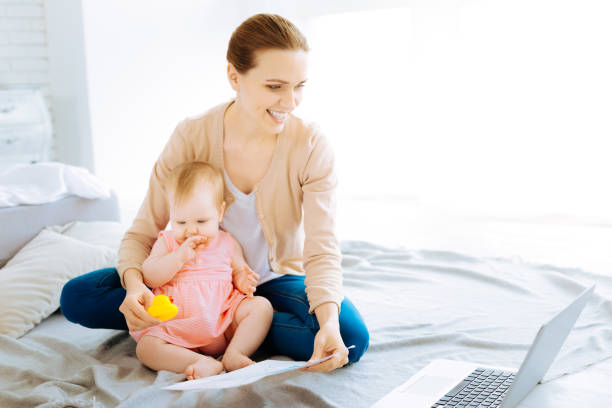 istock Cheerful mother sitting with a child on a bed while working 866926370