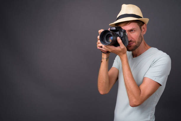 istock Blond bearded tourist man with camera wearing hat against gray background 866939856