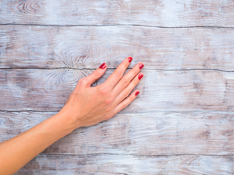 Hand of a woman with red polish on wooden textured surface