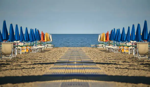 Perfectly specular and symmetrical view of the beach with umbrellas and loungers of Lignano sabbia d'oro in Italy. A scene devoid of people who give emotions of calm and peace as only the sea can do.