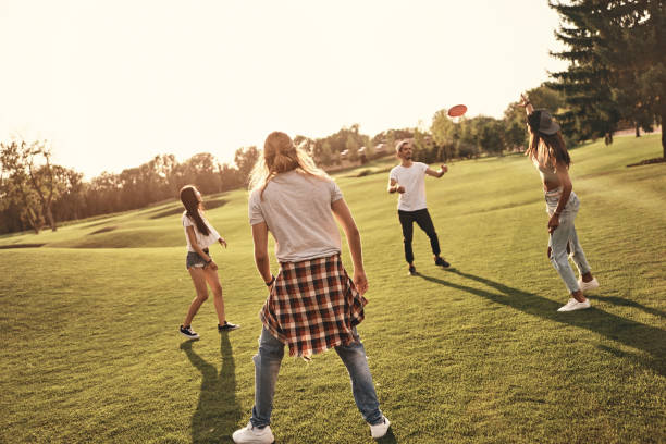 Having fun with friends. Full length of young people in casual wear playing frisbee while spending carefree time outdoors plastic disc stock pictures, royalty-free photos & images