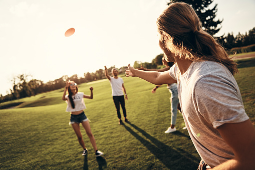 Group of young people in casual wear playing frisbee while spending carefree time outdoors