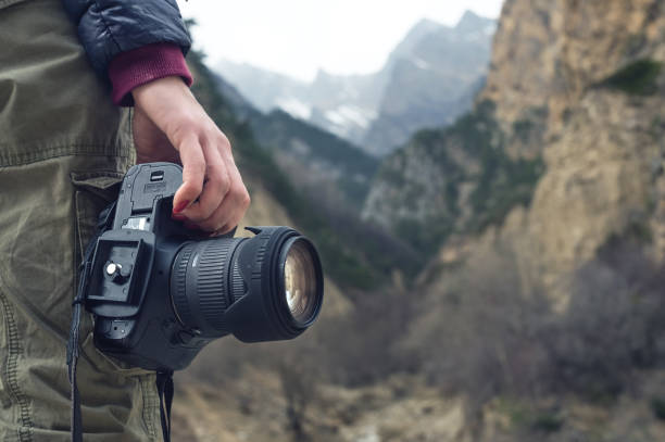 A female hand holds a camera against a mountain landscape stock photo