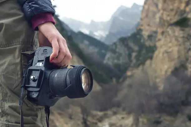 Photo of A female hand holds a camera against a mountain landscape