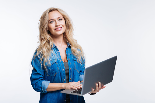 Favorite device. Beautiful fair-haired young woman in a denim shirt posing with a laptop while standing isolated on a white background