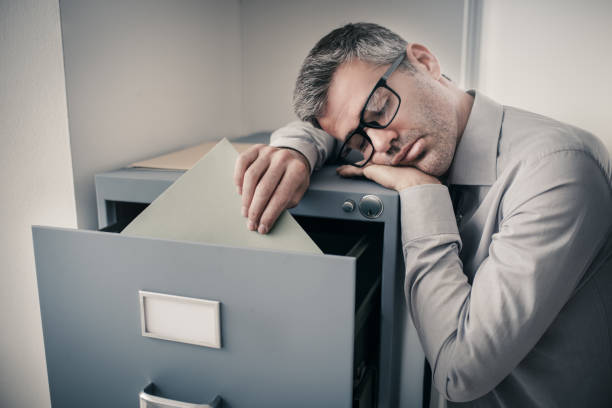 Tired office worker sleeping in the office Tired lazy office worker leaning on a filing cabinet and sleeping, he is falling asleep standing up; stress, unproductivity and sleep disorders concept narcolepsy stock pictures, royalty-free photos & images