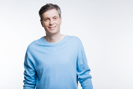 Incarnate of masculinity. The portrait of a handsome middle-aged man in a blue pullover posing against a white background