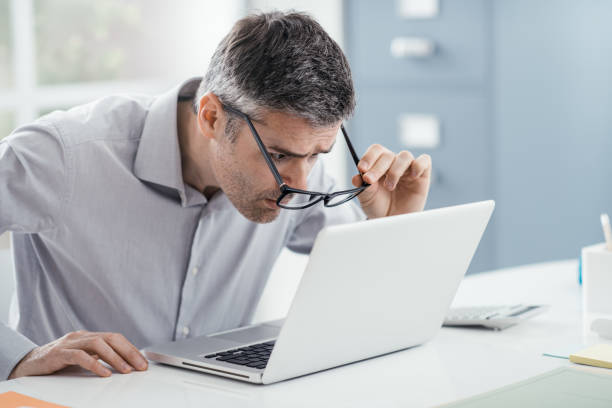 Workplace vision problems Businessman working at office desk, he is staring at the laptop screen close up and holding his glasses, workplace vision problems reading glasses stock pictures, royalty-free photos & images