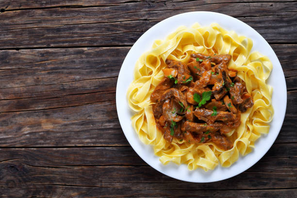 tasty pasta with beef stroganoff stew fettuccine topped with delicious beef stroganoff stew in sour cream sauce with porcini mushrooms on white plate on old dark wooden boards, view from above Cepe stock pictures, royalty-free photos & images