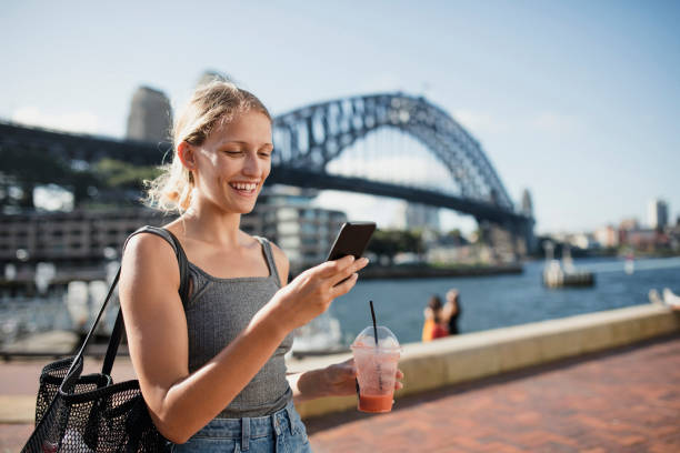 Visiting Sydney A woman uses her phone with a view of Sydney Harbour Bridge in the background. sydney harbor photos stock pictures, royalty-free photos & images