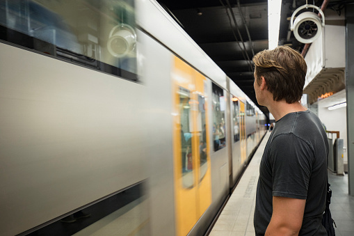 A young man stands on the platform and watches as his train arrives in Sydney.