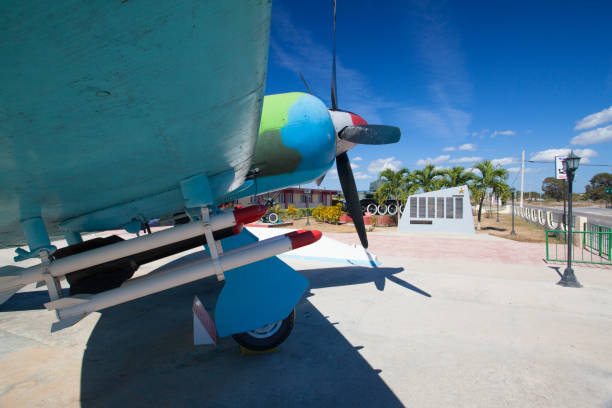 The photo, taken at eye level, depicts the famous Curtiss P-40 fighter which was flown by the American Volunteer Group (AVG) in China during World War II.   The view is of the front left quarter of the airplane which is parked in front of a hangar. The air group, known as the Flying Tigers,  was made up of volunteer American pilots who flew for China to fight against the invading Imperial Army of Japan.  The close up image features deep details of the fighter painted in rich camouflage colors of forest green and medium brown.  The air group, and aircraft, became famous for its menacing shark teeth paint scheme.  The Flying Tigers have become an iconic symbol of WWII.  The photo was shot at Paine Field, WA.