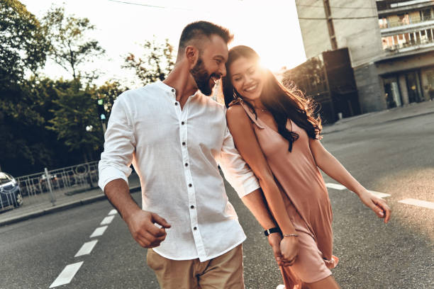 Her happiness is everything to him. Beautiful young couple holding hands and smiling while walking through the city street young couple stock pictures, royalty-free photos & images