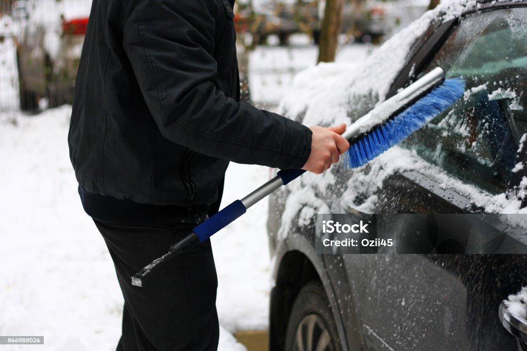 Snowy winter. Snowy winter. The snow machine. A man cleans snow from the car with the help of special brushes. Car Stock Photo