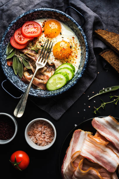 istock Breakfast set. Pan of fried eggs with bacon, fresh tomato, cucumber, sage and bread 867014916