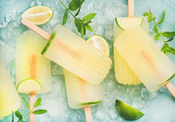 Summer lemonade popsicles with lime and chipped ice, top view Summer refreshing lemonade popsicles with lime and mint with chipped ice over blue background, top view flavored ice photos stock pictures, royalty-free photos & images