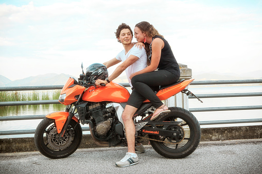 A young italian couple hanging out with their motorbike at Lake Massaciuccoli, in Torre di Lago , northern Tuscany. Italy on a summerday in 2014.  - this is a popular spot for young dating couples in Tuscany.