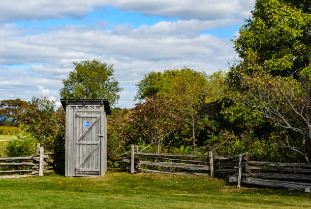Rustic public outhouse at theedge of a park, with split-rail cedar fences and a blue clouded sky. Rustic public outhouse at theedge of a park, with split-rail cedar fences and a blue clouded sky. Outhouse stock pictures, royalty-free photos & images