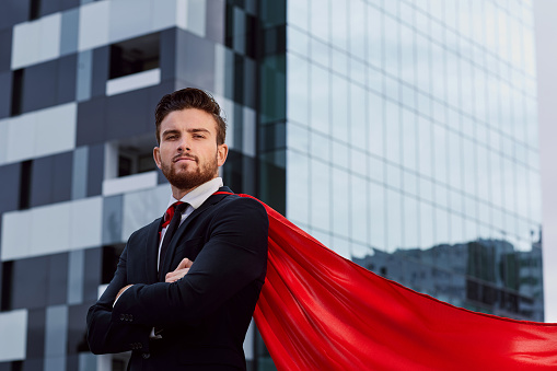 Businessman in a superhero costume against a business building background.