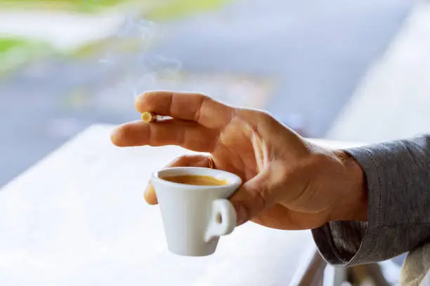 Cigarette in Male Hand With a Cup of Coffee. Smoking Addiction Concept.