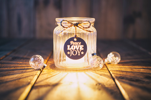 Cute christmas decoration with a light in a jar and some christmas ornaments. Jar is decorated with a bow and a label with the words peace pove and joy.