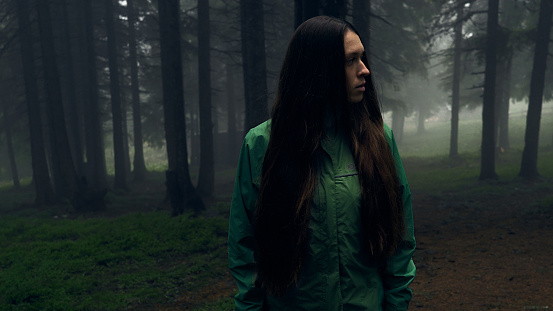 Woman in gloomy mystical forest - thriller scene. Wide-angle lens. Close-up