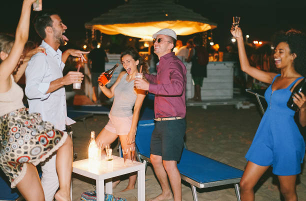 amici felici che fanno festa serale in spiaggia con cocktail e champagne - giovani pazzi che si divertono a ballare e bere - concentrati sulla donna centrale che tiene la bottiglia - concetto di vita notturna - filtro vsco - spanish culture flash foto e immagini stock