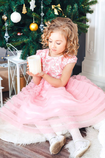 блондинка в розовом платье под елку и смотрит на горящую свечу - flower gift decoration domestic room стоковые фото и изображения