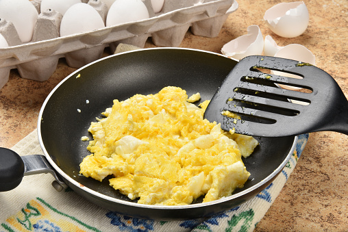 Scrambled eggs in a frying pan near the egg carton