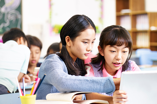 two asian elementary school girls looking at tablet computer thinking hard while working in groups.