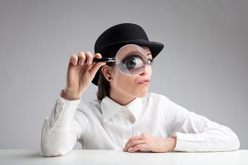 woman in a bowler hat with her eye made big behind a great magnifier meaning suspicion or look for information