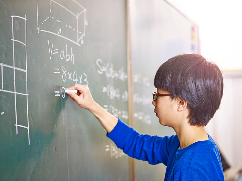 asian grade school student solving a geometry problem on chalkboard in math class.