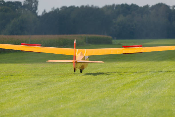 Yellow glider in landing just before the head wheel hits the grass field