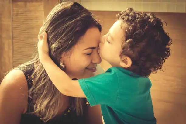 Little 2 years old boy, hugging and kissing his mother, with affectionate gesture.