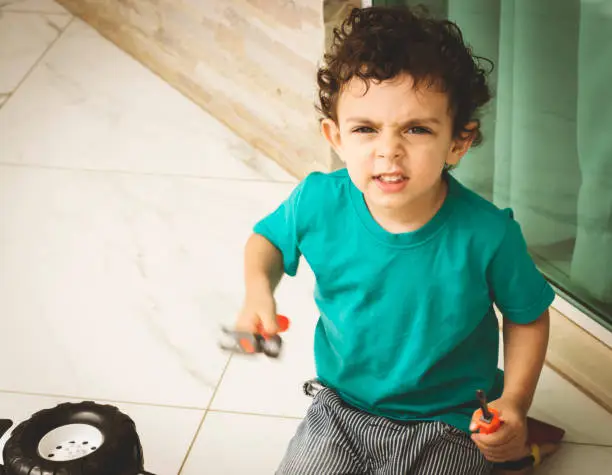 Cute little boy sitting on the floor, holding a toy hammer and a toy screwdriver and looking at camera.