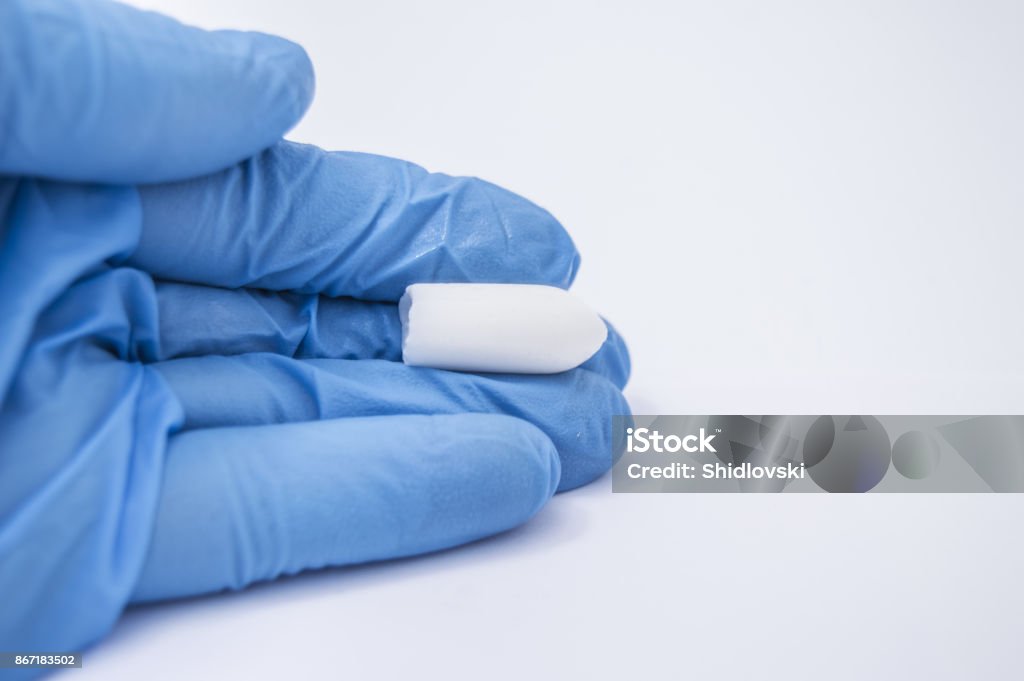 Soft suppository with medicine (laxative or to treat proctological diseases) lies in the hand of the doctor proctologist that dressed in blue medical glove Suppository Stock Photo