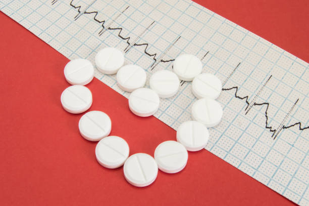 Shape of the human heart, composed of white pills lies on electrocardiogram on homogeneous red background. Heart of pills - idea of diagnostic imaging and treatment of cardiac diseases in cardiology forma del corazón humano, compuesto de píldoras blancas se encuentra en electrocardiograma en fondo rojo homogéneo. corazón de píldoras - idea de la proyección de imagen de diagnóstico y tratamiento de enfermedades cardíacas en cardiología