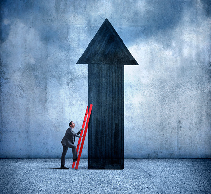 A businessman uses a red ladder as he leans it against a tall arrow pointing in an upward direction as he prepares to climb it.