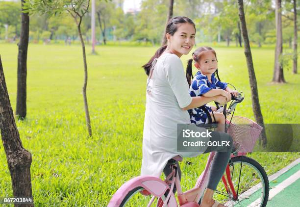 Asian Mother And Her Child Girl On A Bike At The Park In The Morning Stock Photo - Download Image Now