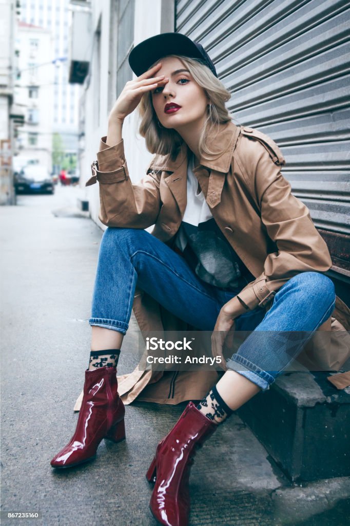Beautiful blonde woman in a coat A young beautiful blonde woman is sitting and enjoying small urban street in Shanghai. She is wearing nice long brown coat and black hat. Her gorgeous face is accentuated by a dark red lipstick. Fashion Stock Photo