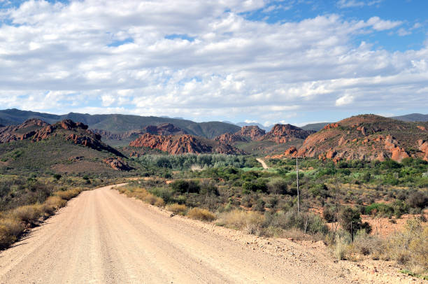 istock Sweeping Dirt Road Leading to Hills Under Cloudy Blue Sky 867235586