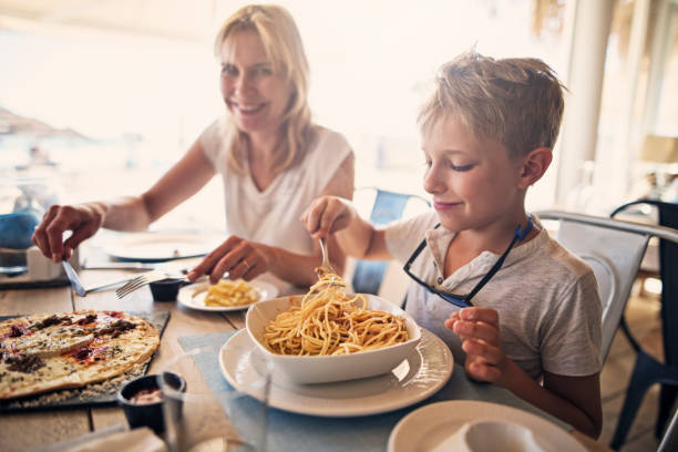 Mother and son enjoying meal in hotel restaurant Mother and son enjoying meal in hotel restaurant. The boy is eating spaghetti and the mother is having a pizza.
kids eating noodles stock pictures, royalty-free photos & images
