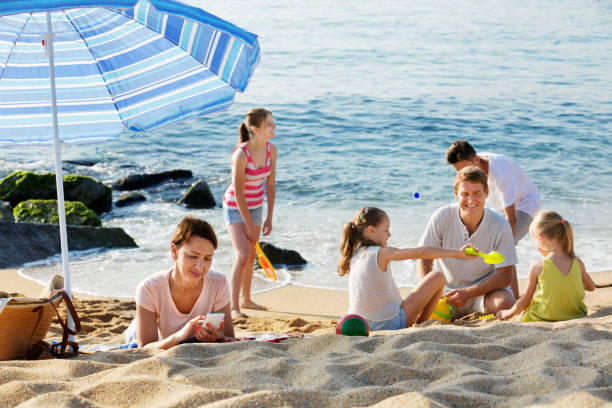 istock Woman looking at her mobile phone while her family  playing on beach 867287860